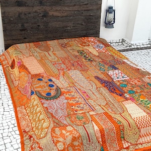 May include: A large, orange and gold patchwork quilt with intricate embroidery and embellishments. The quilt is made up of many different fabrics and patterns, creating a unique and colorful design.