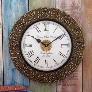 May include: A gold-toned wall clock with a black face and Roman numeral markings. The clock face features the text "Royal Clock Works Birmingham estd. 1792". The clock is surrounded by a decorative floral design.