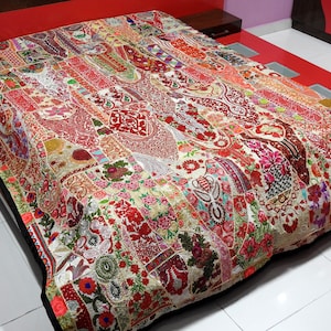 May include: A colourful patchwork quilt, featuring a mix of red, pink, and cream hues. The quilt showcases a variety of floral and paisley designs, creating a rich, textured appearance. The quilt is spread across a bed.