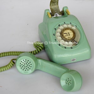 May include: A vintage green rotary dial phone with a coiled cord and a handset. The phone has a white dial with black numbers and a white label with the text "OKI" on it.