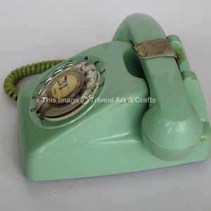 May include: A vintage rotary dial phone in a pale green colour. The phone has a coiled cord and a rotary dial with numbers 0-9. The phone is in good condition with some signs of wear.