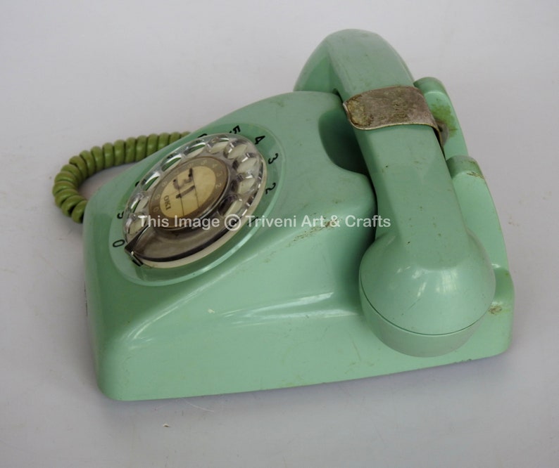 May include: A vintage rotary dial phone in a pale green colour. The phone has a coiled cord and a rotary dial with numbers 0-9. The phone is in good condition with some signs of wear.