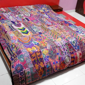 May include: A colourful patchwork quilt featuring a range of fabrics and embroidery. The quilt is made up of many different colours and patterns, including floral, geometric, and paisley designs. The quilt is laid out on a bed.