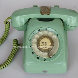 May include: A vintage green rotary dial phone with a white dial and black numbers. The phone has a coiled green cord.