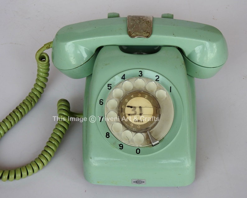 May include: A vintage green rotary dial phone with a white dial and black numbers. The phone has a coiled green cord.