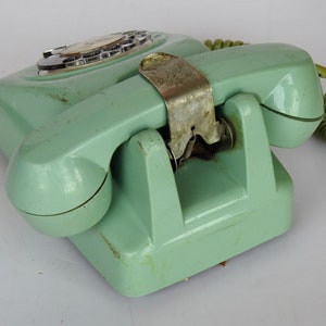 May include: A vintage rotary dial phone in a pale green colour with a matching handset and a coiled cord. The phone has a metal cradle and a rotary dial with numbers 0-9.