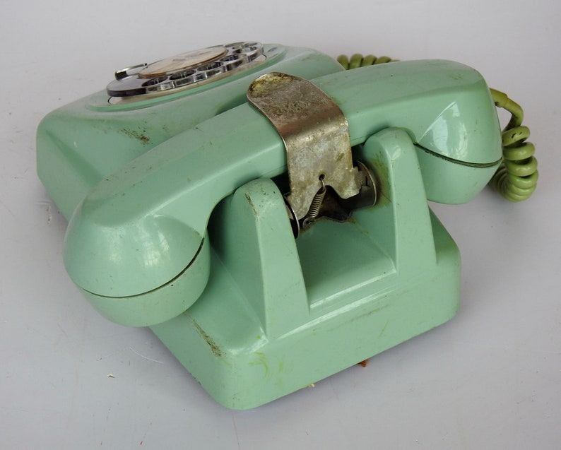 May include: A vintage rotary dial phone in a pale green colour with a matching handset and a coiled cord. The phone has a metal cradle and a rotary dial with numbers 0-9.