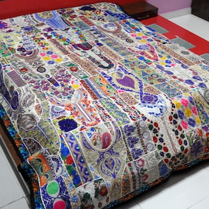 May include: A white patchwork quilt with colorful embroidery and embellishments. The quilt is made of various fabrics and textures, including velvet, silk, and cotton. It features a variety of patterns and designs, including floral motifs, geometric shapes, and traditional Indian embroidery.