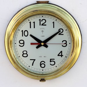 May include: A gold-colored round clock with black hands and white face. The clock face has black numbers 1 through 12, and the words "POLARIS", "北极星", and "中国烟台" are printed on the face.
