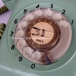 May include: A vintage green rotary dial phone with a white dial and black numbers. The phone has a silver push button and the text "OKI" is visible on the dial.