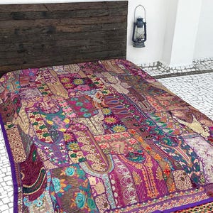 May include: A purple and gold patchwork quilt with intricate embroidery and sequins. The quilt is made of various fabrics and textures, creating a unique and bohemian style.