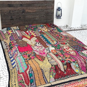 May include: A colorful patchwork quilt with a black border, featuring a variety of fabrics in shades of red, pink, yellow, and blue. The quilt is placed on a bed with a dark wooden headboard. Two vintage lanterns hang on the wall.