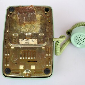 May include: A vintage green rotary phone with a coiled cord and a label on the bottom that reads "ODA-1150-1 DATE".