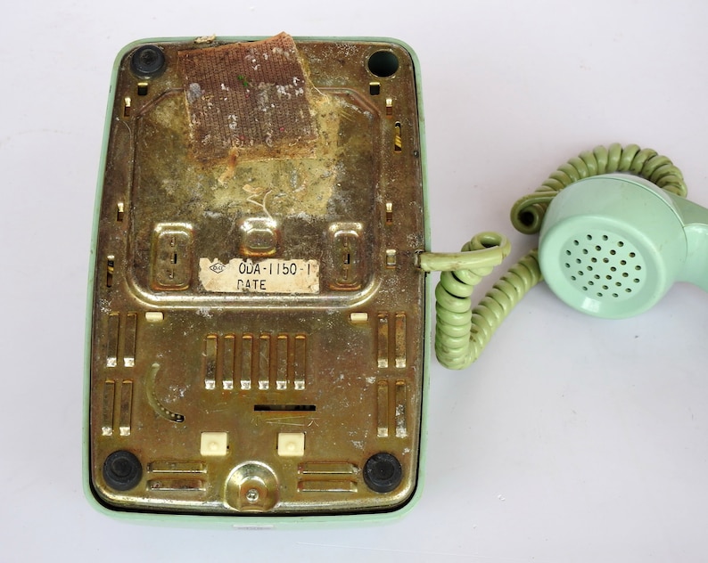 May include: A vintage green rotary phone with a coiled cord and a label on the bottom that reads "ODA-1150-1 DATE".