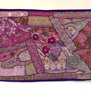 May include: A colourful patchwork wall hanging with a purple border. The fabric is decorated with sequins, beads, and embroidery. The design features a variety of floral and geometric patterns.