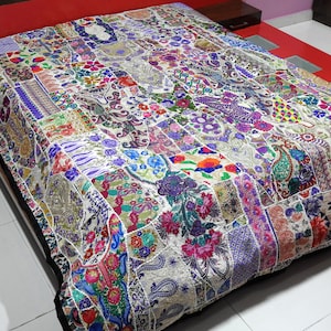 May include: A white patchwork quilt with a black border. The quilt is made of many different fabrics and colours, including purple, blue, green, red, and yellow. The quilt is embroidered with floral designs.
