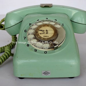 May include: A vintage green rotary dial phone with a white dial and black numbers. The phone has a gold-coloured label that says "OKI" and the text "This Image &copy; Triveni Art & Crafts".