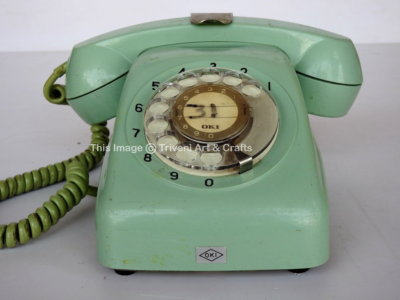 May include: A vintage green rotary dial phone with a white dial and black numbers. The phone has a gold-coloured label that says "OKI" and the text "This Image &copy; Triveni Art & Crafts".