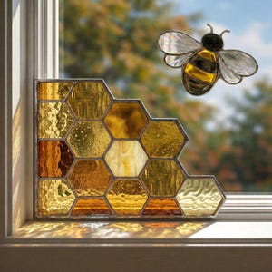 May include: A stained glass window panel in a honeycomb design with shades of gold and amber. A decorative bee with translucent wings is positioned near the window. The panel is set in a window frame, with sunlight casting shadows.