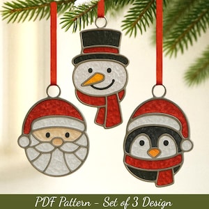 Op de afbeelding: Drie kerstversieringen: een sneeuwpop, de kerstman en een pinguïn, elk met een rood-wit ontwerp en een zwarte omtrek. Ze hangen aan rode linten die aan een groene tak zijn bevestigd. De tekst "PDF Pattern - Set of 3 Design" staat onderaan.