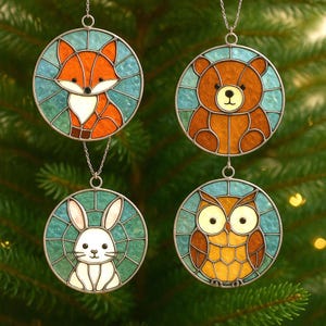 May include: Four stained glass ornaments with woodland animal designs: a fox, bear, rabbit, and owl. Each ornament is round, with a silver-colored metal frame and a chain for hanging. The animals are depicted in vibrant colors against a teal and green background.