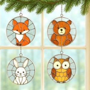 Puede incluir: Cuatro adornos redondos de ventana de vidrieras con animales del bosque: un zorro, un oso, un conejo y un búho. Cada adorno tiene un marco de metal plateado y un fondo azul claro. El zorro es naranja y blanco, el oso es marrón, el conejo es blanco y el búho es amarillo y marrón.