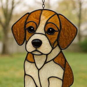 May include: Stained glass puppy dog suncatcher with brown and white panels, black outlines, and a chain for hanging. The dog has large, dark eyes and a black nose. The suncatcher is designed to be displayed in a window or as a decorative piece.