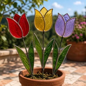 Könnte beinhalten: Drei Glasmalerei-Tulpen in einem Terrakotta-Topf. Die Tulpen sind rot, gelb und lila mit grünen Blättern und dunklen Stielen. Die Blumen werden im Freien ausgestellt.