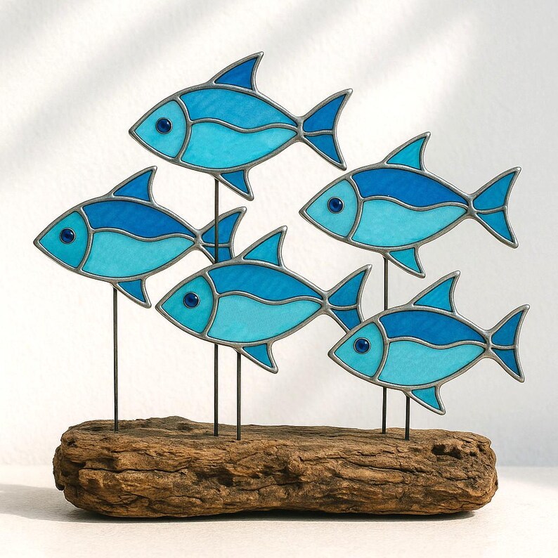 Puede incluir: Una escultura decorativa con cinco peces de vidrieras azules montados sobre varillas met&aacute;licas individuales, colocados en un trozo de madera flotante. Los peces tienen diferentes tonos de azul y est&aacute;n acentuados con ojos azul oscuro y contornos plateados.
