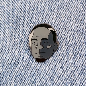 May include: Black and white enamel pin of a person's face. The face is split down the middle, with one side black and the other white.