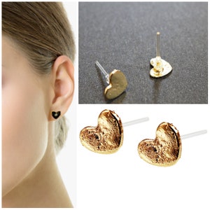 May include: A pair of gold heart-shaped stud earrings with a textured finish. The earrings are on a white background.