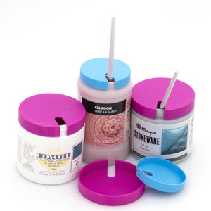 May include: Three ceramic glaze jars with lids in pink and blue. One jar is labeled "CELADON CONE 5-6 GLAZES 16 fl oz (472 ml)". Another jar is labeled "COYOTE CLAY & COLOR ALMOST TEAL MBG001-P 1 Pint". The third jar is labeled "Mayco STONEWARE SW-166 Norse Blue".