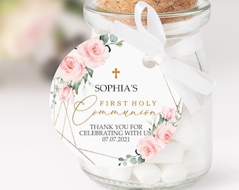 May include: A round favor tag with a gold cross, pink flowers, and greenery. The tag says "Sophia's First Holy Communion" and "Thank you for celebrating with us 07.07.2021".