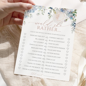 May include: A blue and white floral bridal shower game card with the text "Would she rather..." and a list of questions for guests to answer about the bride. The card has a pink heart design.