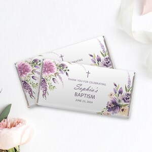Puede incluir: Dos envoltorios de barra de chocolate blanco con un diseño floral en tonos morados y blancos. El texto en el envoltorio dice "Gracias por celebrar el bautismo de Sophia el 23 de junio de 2024".