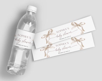 May include: Two white water bottle labels with a brown ribbon bow design. The text on the labels reads "Sophia's baby shower" with the date "01.15.2026" and location "Key West, FL".