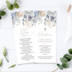 May include: A white card with blue floral designs and a cross. The card has the text "Lord Hear My Prayer" and a prayer. The card also has the text "Christina's First Holy Communion July 15th" and a prayer.