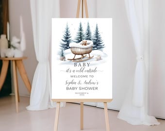 Może przedstawiać: Zaproszenie na baby shower w zimowym stylu z uroczym pluszowym misiem w saniach otoczonym śnieżnymi sosnami. Tekst brzmi "BABY jest zimno na zewnątrz WITAMY Sophia & Andrew's BABY SHOWER 16 GRUDNIA 2026".