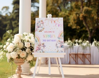 May include: A white sign with a unicorn theme welcomes guests to Sophia's 3rd birthday party. The sign features a rainbow, stars, and two unicorns. The sign is displayed on a white easel.