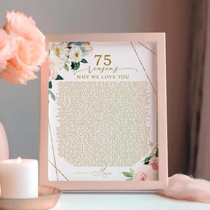 May include: A rectangular picture frame with a light pink border containing a printed list titled 75 reasons WHY WE LOVE YOU in gold lettering, decorated with white and pink floral illustrations and gold geometric lines, personalised with the name Marie.