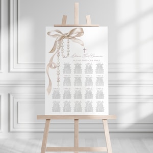 May include: A white seating chart with a pearl and ribbon design. The chart is titled "Allison's First Communion" and includes the text "Please find your table".