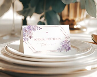 May include: A white place card with a gold geometric frame and purple floral accents. The text on the card reads "Sophia Jefferson, Table One" with a small cross symbol above the name.