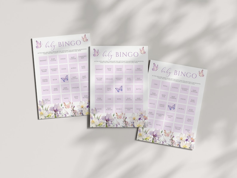 May include: Three purple and white baby bingo cards with a floral and butterfly design. The cards have a grid of squares with baby-related items listed in each square. The text on the cards reads "baby bingo".