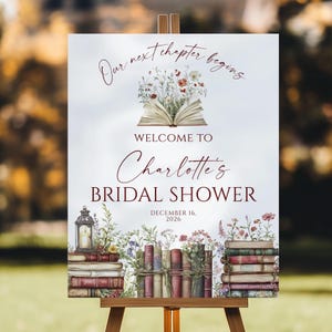 Peut inclure: Panneau sur chevalet avec le texte "Our next chapter begins" et "Welcome to Charlotte's Bridal Shower". Le panneau présente un livre ouvert avec des fleurs, des piles de livres et une lanterne. La date "December 16, 2026" est également affichée.