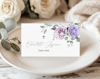 May include: A white place card with floral watercolor design, featuring lavender and purple roses, and eucalyptus leaves. The card has the name "Charlotte Jefferson" and "Table One" printed on it. The card is placed on a white plate.
