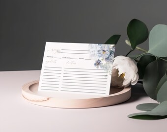 May include: A blank recipe card with a floral design featuring blue and white flowers. The card has lines for writing down ingredients, instructions, prep time, cook time, and servings.