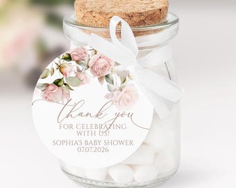 Könnte beinhalten: Ein klares Glas mit einem Korken, gefüllt mit weißen Süßigkeiten. Ein rundes Etikett mit rosa Rosen und dem Text "Thank you" ist mit einem weißen Band an dem Glas befestigt. Das Etikett enthält auch den Text "FOR CELEBRATING WITH US!" und "SOPHIA'S BABY SHOWER 07.07.2026".