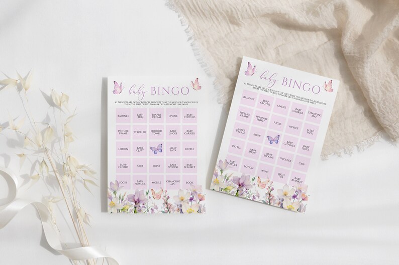 May include: Two pink and purple baby shower bingo cards with a floral and butterfly design. The cards have a list of baby-related items to check off during the shower.