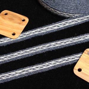 May include: Three black and white woven straps with a diamond pattern on a black background. Two square wooden pieces with holes in the corners are placed on the straps.