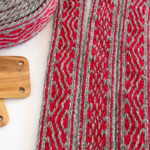 May include: Two woven grey and red wool bands with a geometric pattern. The bands are flat and have a smooth texture.